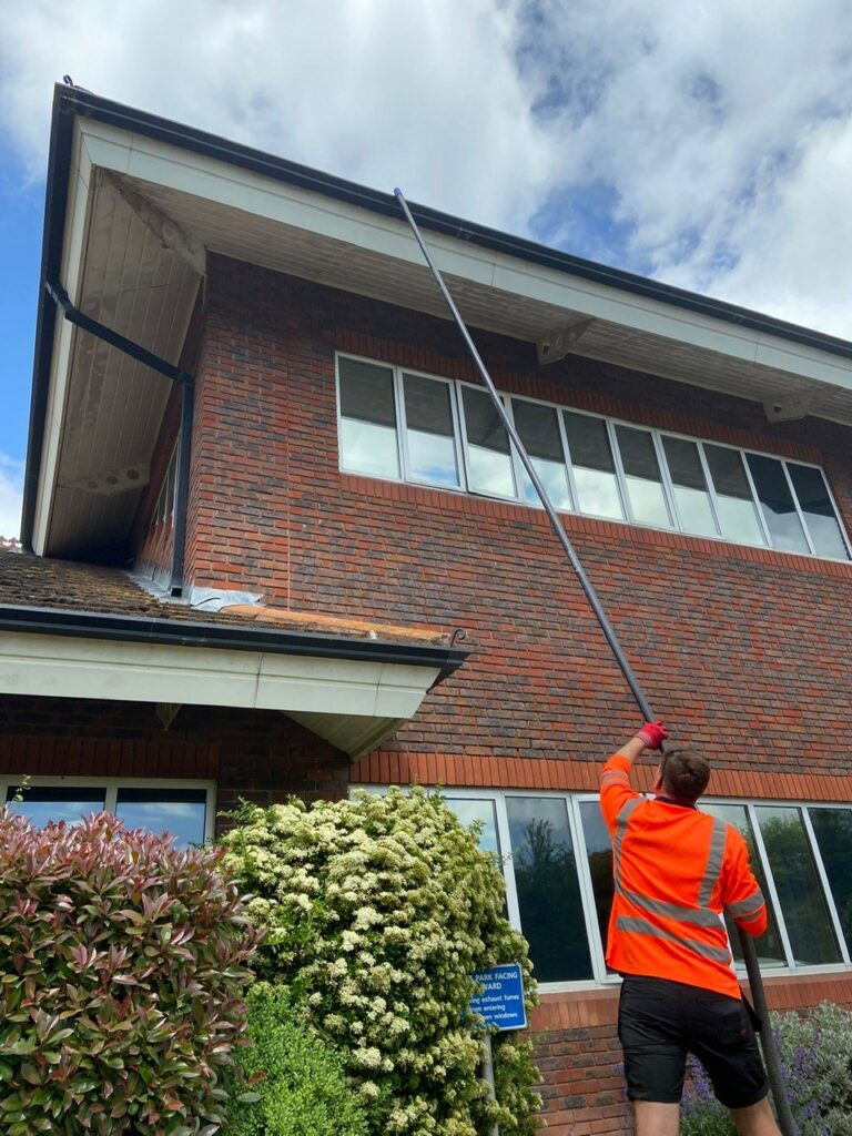 A Coastal Drains worker cleaning hospital gutters with a long reach pole vacuum